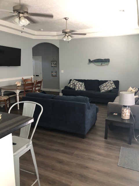 living room with dark wood-type flooring, ceiling fan, and a raised ceiling