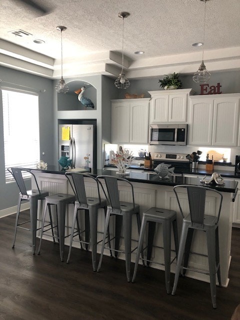 kitchen featuring appliances with stainless steel finishes, white cabinetry, pendant lighting, and dark hardwood / wood-style flooring