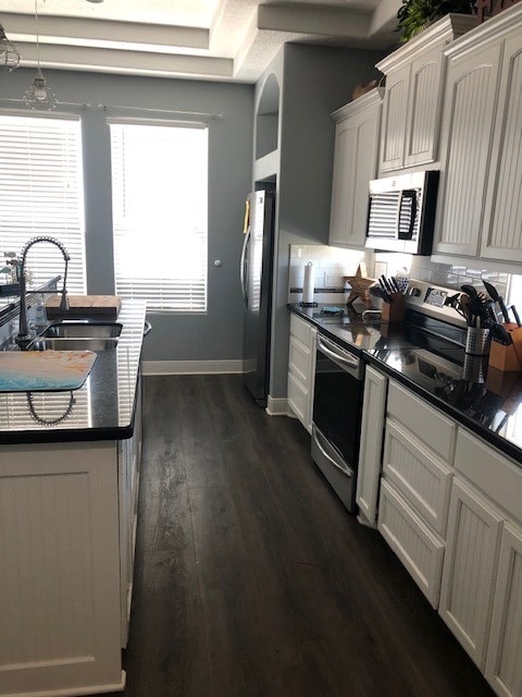 kitchen featuring dark hardwood / wood-style floors, stainless steel appliances, backsplash, sink, and white cabinetry