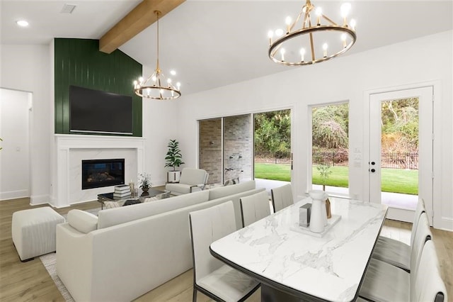 dining area with a notable chandelier, a wealth of natural light, a fireplace, lofted ceiling with beams, and light hardwood / wood-style floors