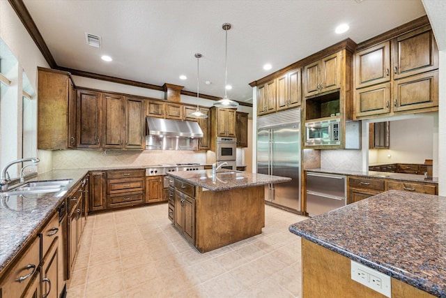 kitchen featuring decorative light fixtures, an island with sink, sink, dark stone countertops, and built in appliances