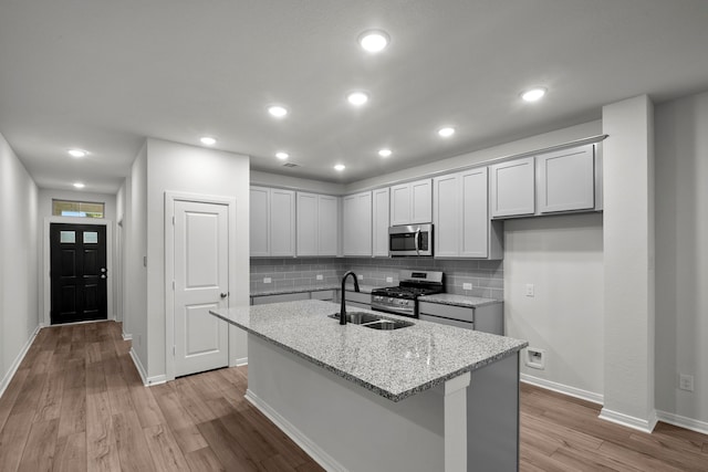 kitchen featuring a center island with sink, appliances with stainless steel finishes, light hardwood / wood-style floors, sink, and light stone counters