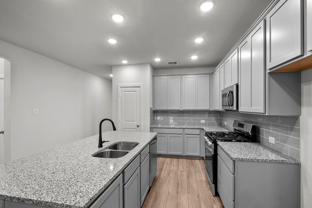 kitchen featuring light stone countertops, appliances with stainless steel finishes, light hardwood / wood-style floors, an island with sink, and sink