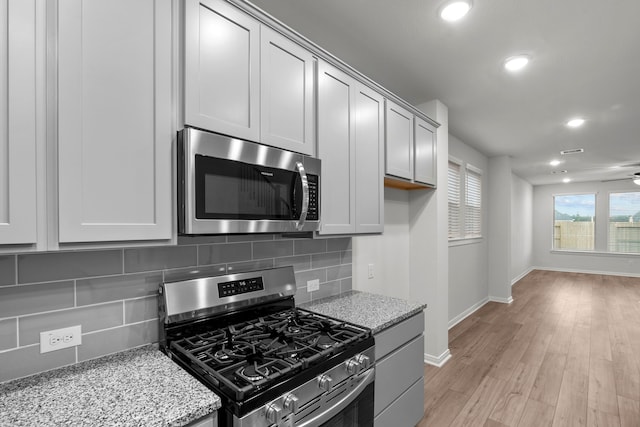 kitchen with light hardwood / wood-style flooring, light stone counters, stainless steel appliances, and decorative backsplash