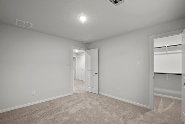 unfurnished bedroom with light colored carpet, a walk in closet, and a closet