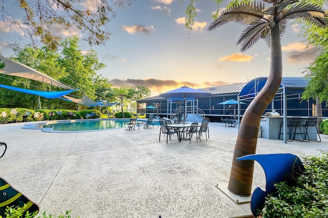 pool at dusk with exterior bar and a patio