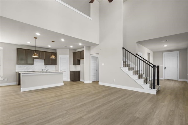 unfurnished living room featuring a towering ceiling, light wood-type flooring, and ceiling fan