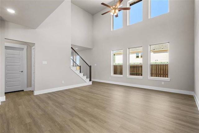 unfurnished living room with a towering ceiling, hardwood / wood-style flooring, and ceiling fan