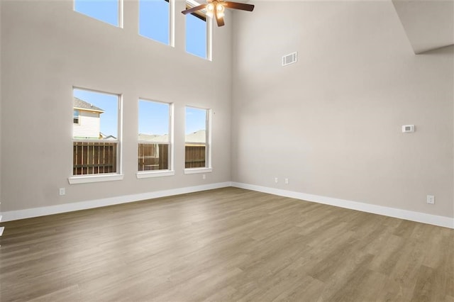 unfurnished living room with ceiling fan, a wealth of natural light, a towering ceiling, and wood-type flooring