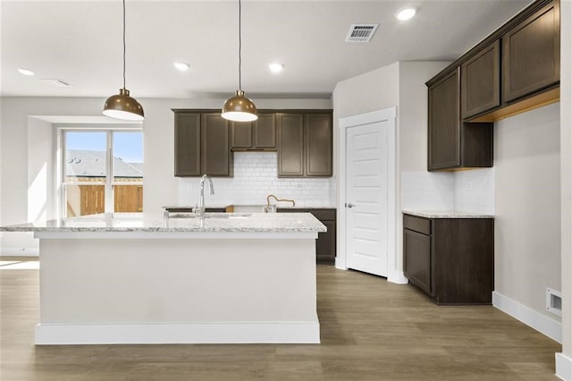 kitchen featuring pendant lighting, light stone counters, a kitchen island with sink, and dark hardwood / wood-style floors