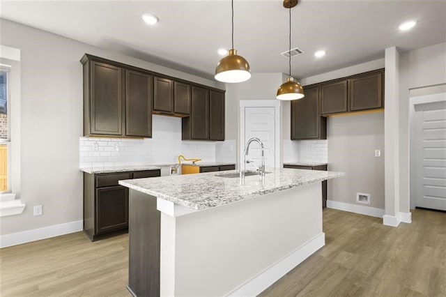 kitchen with a center island with sink, light hardwood / wood-style floors, hanging light fixtures, and sink