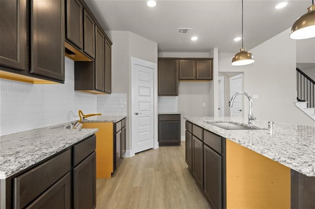 kitchen with an island with sink, decorative backsplash, sink, light hardwood / wood-style flooring, and decorative light fixtures