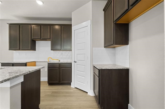 kitchen with dark brown cabinets, light stone countertops, light hardwood / wood-style floors, and tasteful backsplash