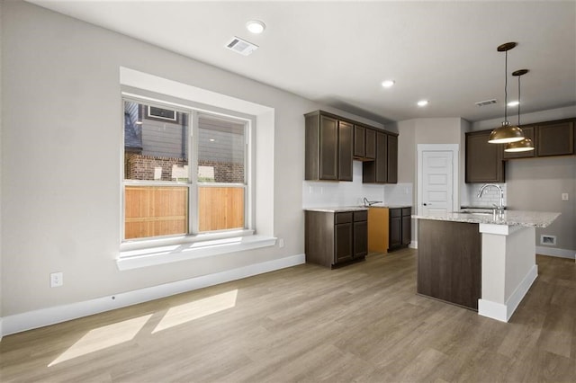 kitchen with pendant lighting, an island with sink, sink, dark brown cabinets, and light hardwood / wood-style floors