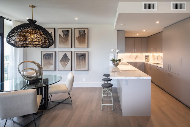 kitchen featuring pendant lighting, tasteful backsplash, light hardwood / wood-style floors, sink, and gray cabinets