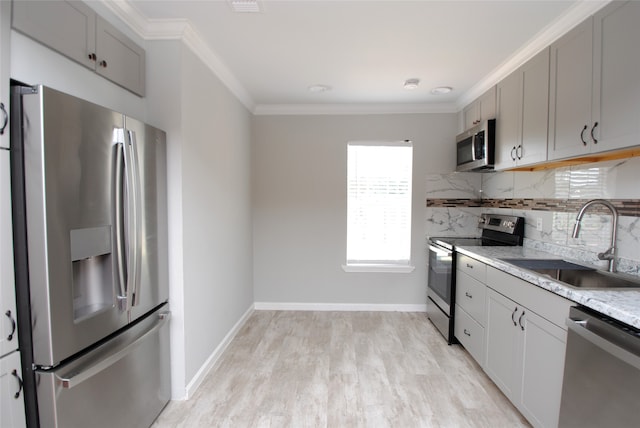 kitchen with light wood-type flooring, gray cabinetry, backsplash, sink, and appliances with stainless steel finishes