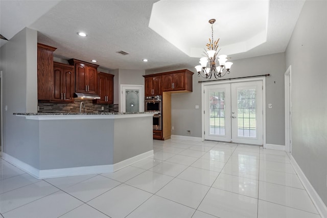 kitchen featuring a notable chandelier, french doors, a tray ceiling, double oven, and dark stone countertops