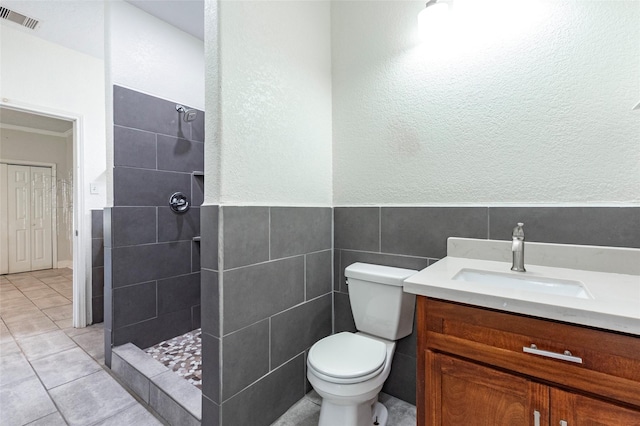 bathroom with toilet, tiled shower, tile patterned floors, vanity, and tile walls