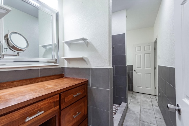 bathroom with tile walls, a shower, tile patterned floors, and vanity