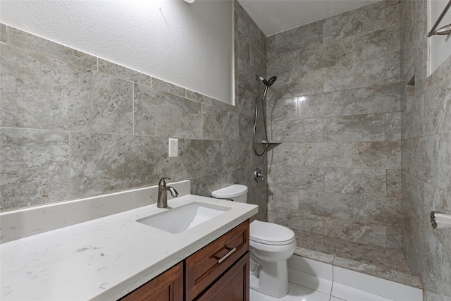 bathroom with a tile shower, toilet, vanity, and tile walls