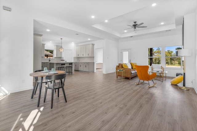 living room featuring a raised ceiling, ceiling fan, light hardwood / wood-style flooring, and sink