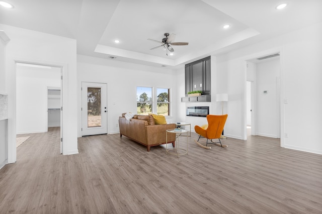 living room featuring a fireplace, a tray ceiling, and light hardwood / wood-style floors