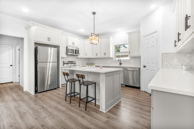 kitchen featuring appliances with stainless steel finishes, a kitchen island, pendant lighting, light hardwood / wood-style floors, and white cabinetry