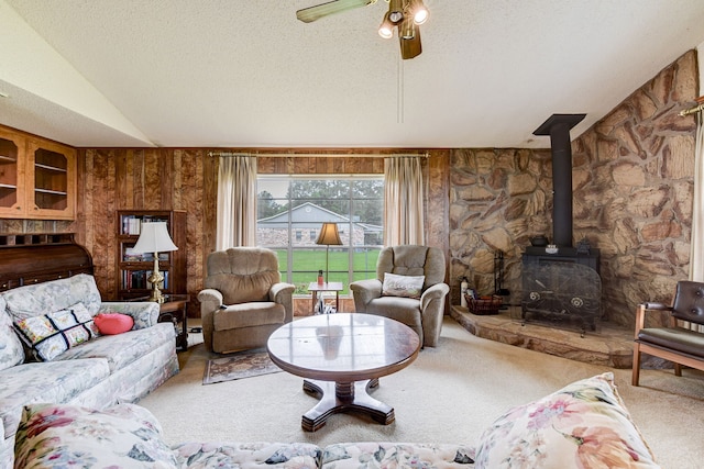 carpeted living room with vaulted ceiling, a wood stove, ceiling fan, and a textured ceiling