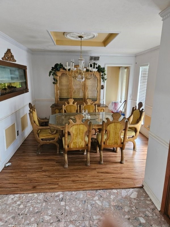 dining space featuring an inviting chandelier, wood-type flooring, crown molding, and a tray ceiling