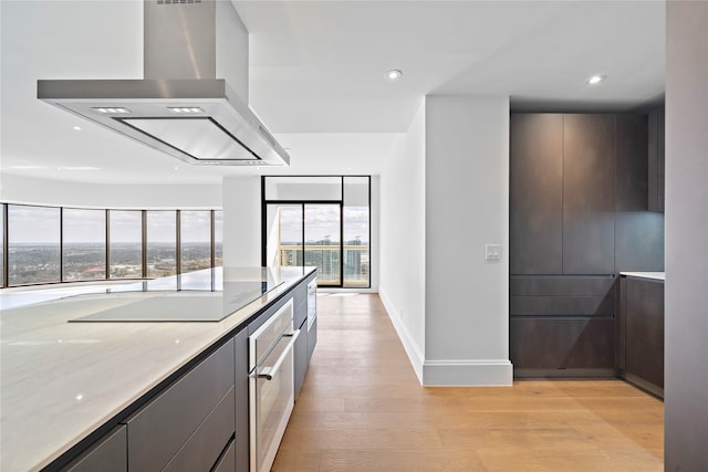 kitchen featuring black electric stovetop, light stone counters, stainless steel oven, ventilation hood, and light hardwood / wood-style floors