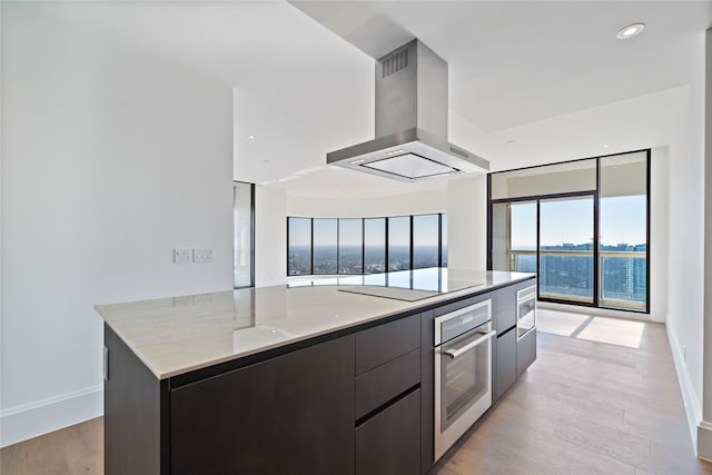 kitchen featuring appliances with stainless steel finishes, a spacious island, island range hood, a water view, and light wood-type flooring