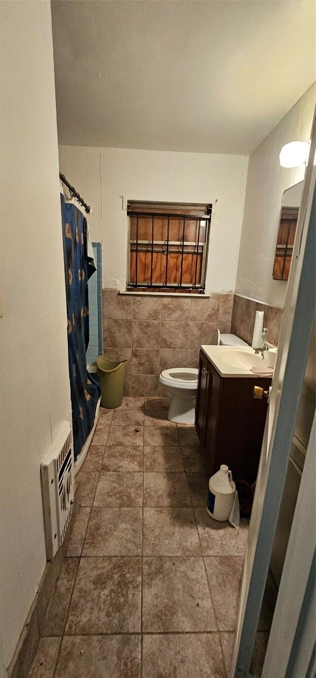 bathroom with tile floors, vanity, toilet, and tile walls