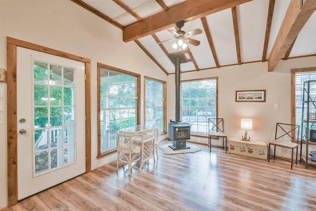 sunroom featuring vaulted ceiling with beams, plenty of natural light, and a wood stove