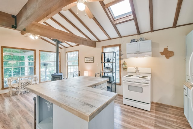 kitchen with a wood stove, white stove, lofted ceiling with skylight, white cabinets, and light hardwood / wood-style floors