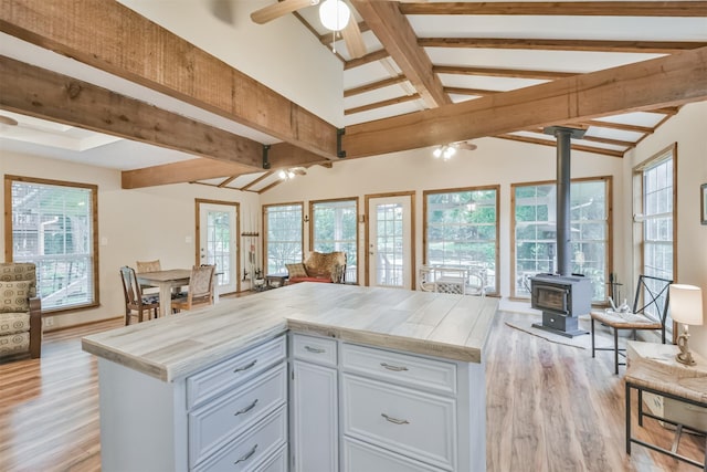 kitchen featuring a wood stove, white cabinets, vaulted ceiling with beams, ceiling fan, and light wood-type flooring