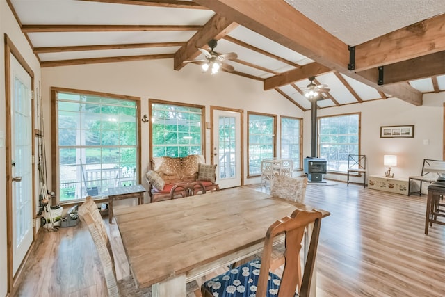 dining area featuring a wood stove, plenty of natural light, lofted ceiling with beams, and light hardwood / wood-style flooring