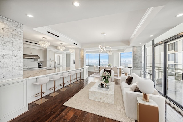 living room with dark hardwood / wood-style floors, sink, crown molding, a notable chandelier, and a raised ceiling