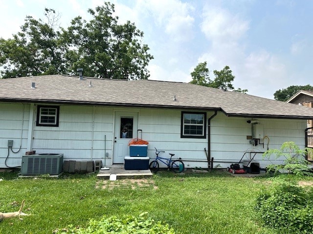 rear view of property with central AC unit and a lawn