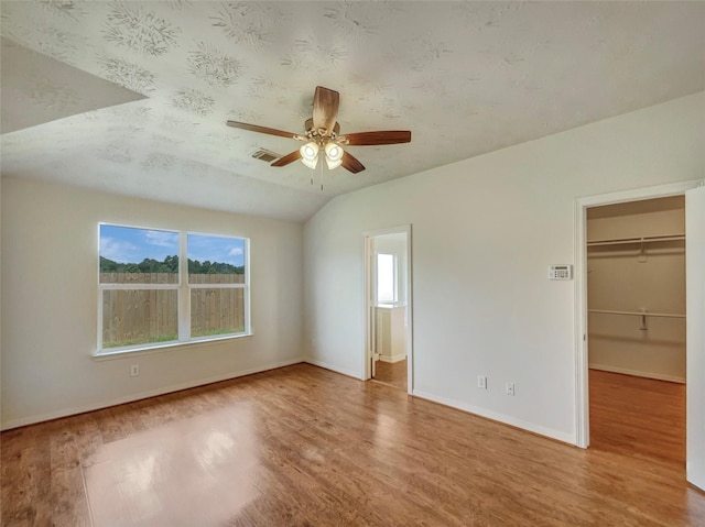 unfurnished bedroom with hardwood / wood-style floors, a walk in closet, vaulted ceiling, ceiling fan, and a closet