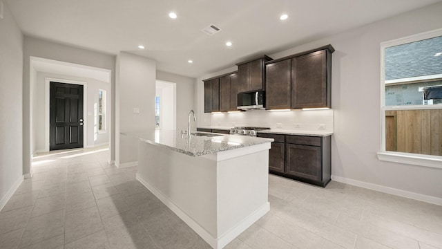 kitchen with light stone countertops, sink, an island with sink, decorative backsplash, and appliances with stainless steel finishes