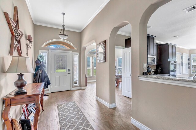 entryway featuring light wood-style flooring, visible vents, arched walkways, and crown molding