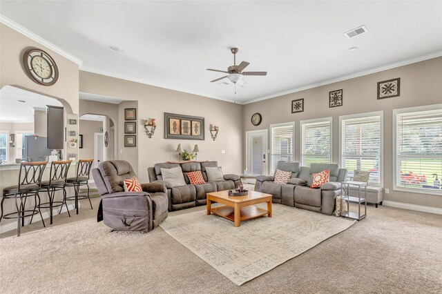 carpeted living area with arched walkways, baseboards, visible vents, and crown molding