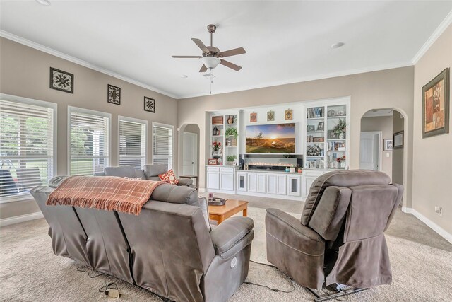 living room with arched walkways, light colored carpet, ornamental molding, ceiling fan, and baseboards