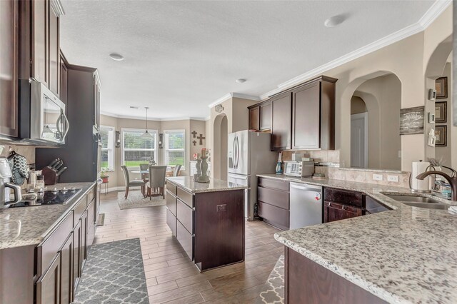 kitchen featuring arched walkways, dark brown cabinetry, stainless steel appliances, a sink, and light stone countertops