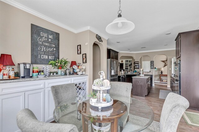 dining area featuring ornamental molding, arched walkways, and wood finished floors