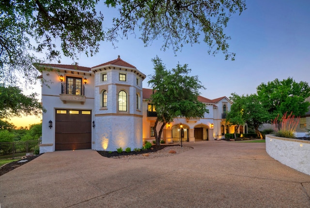 mediterranean / spanish-style house featuring driveway, a balcony, a tile roof, and fence