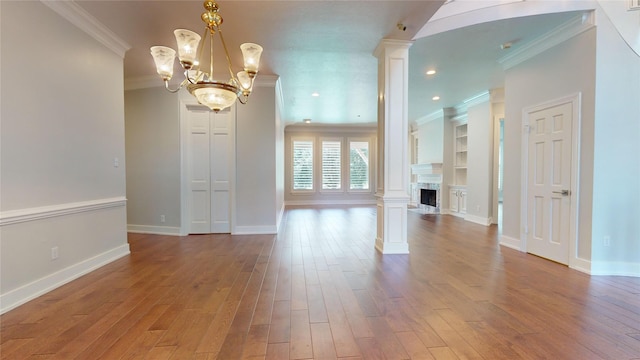 unfurnished living room featuring hardwood / wood-style floors, decorative columns, crown molding, and an inviting chandelier