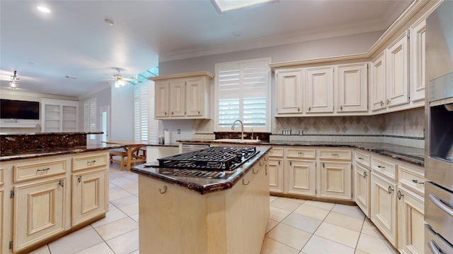 kitchen featuring ceiling fan, a center island, crown molding, cream cabinets, and decorative backsplash