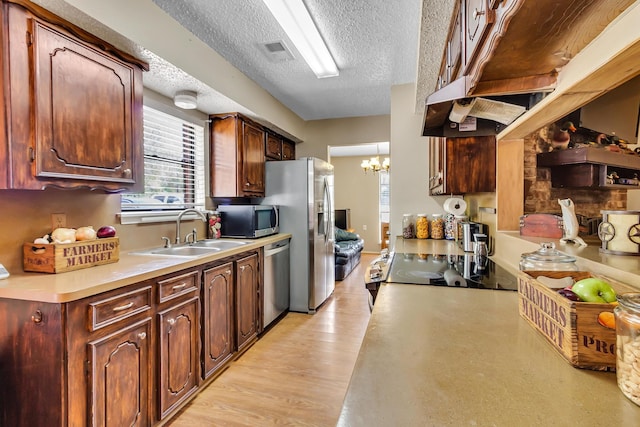 kitchen featuring sink, light hardwood / wood-style flooring, a chandelier, a textured ceiling, and appliances with stainless steel finishes