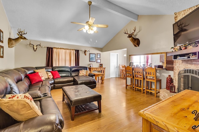 living room with light wood-type flooring, a fireplace, a textured ceiling, ceiling fan, and beamed ceiling